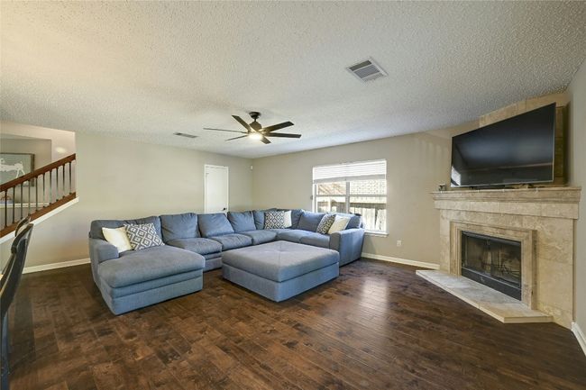 Living area with wood-type flooring, a ceiling fan, a textured ceiling, a fireplace, and stairway | Image 9