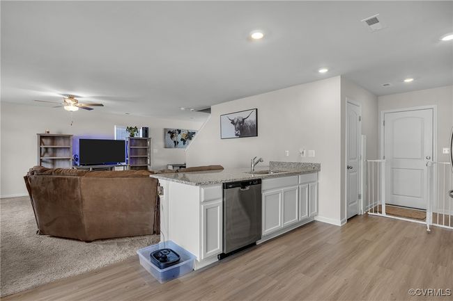 Kitchen with white cabinetry, stainless steel dishwasher, a sink, light stone counters, and a peninsula | Image 7