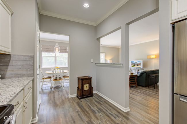 kitchen with appliances with stainless steel finishes, laminate floors, white cabinets, crown molding, and light stone countertops | Image 12