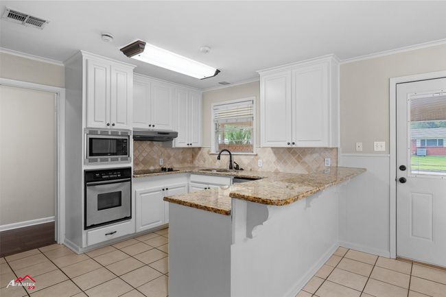 Kitchen with stainless steel appliances, a sink, crown molding, light tile patterned floors, and white cabinets | Image 5