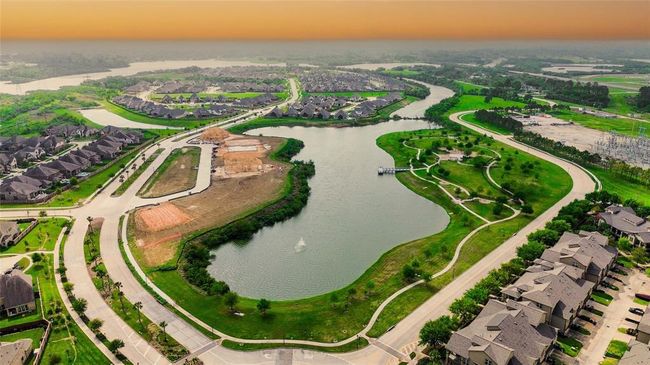 This aerial photo showcases a serene residential neighborhood featuring a winding lake, surrounded by well-maintained homes and lush greenery. Curved roads and walking paths enhance the picturesque setting, ideal for families seeking a tranquil and scenic living environment. | Image 46