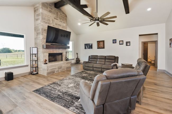 Living area with ceiling fan, a stone fireplace, beam ceiling, wood finished floors, and high vaulted ceiling | Image 16
