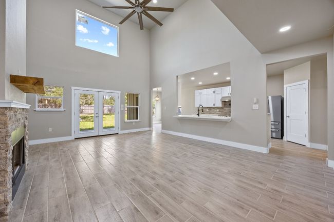 Unfurnished living room with light wood-style floors, baseboards, a ceiling fan, and a stone fireplace | Image 4