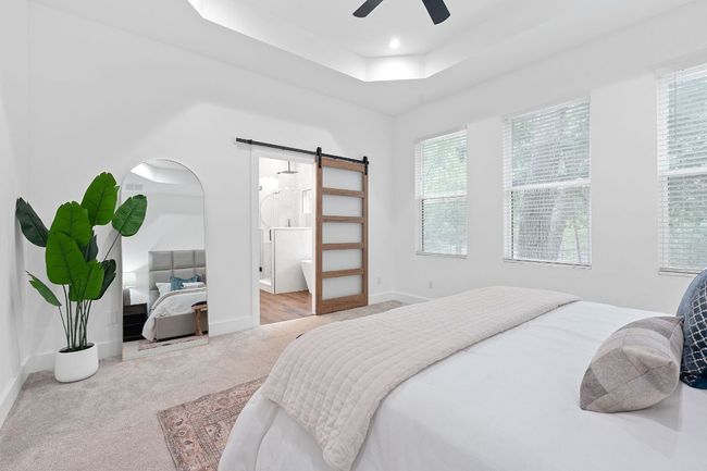 Carpeted bedroom with a tray ceiling, a barn door, baseboards, and multiple windows | Image 25