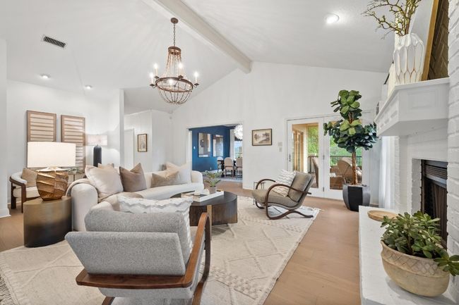 Living area featuring light wood finished floors, a chandelier, high vaulted ceiling, a fireplace, and beam ceiling | Image 8