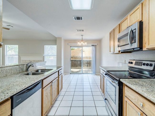 Kitchen with appliances with stainless steel finishes, light brown cabinetry, a chandelier, light tile patterned floors, and light stone countertops | Image 15