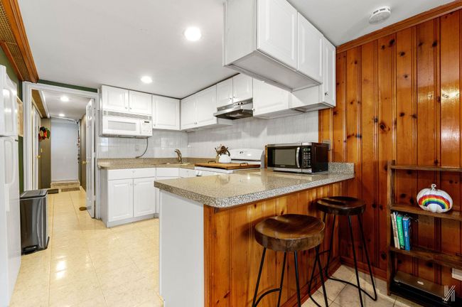 Kitchen with white appliances, under cabinet range hood, a sink, a peninsula, and white cabinetry | Image 13