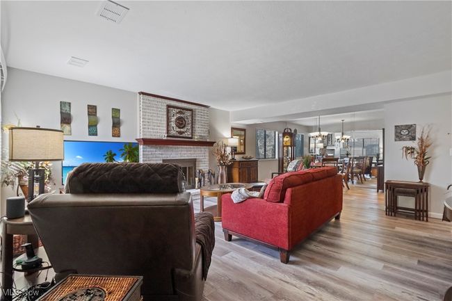 Living room with visible vents, an inviting chandelier, light wood-style floors, and a brick fireplace | Image 12