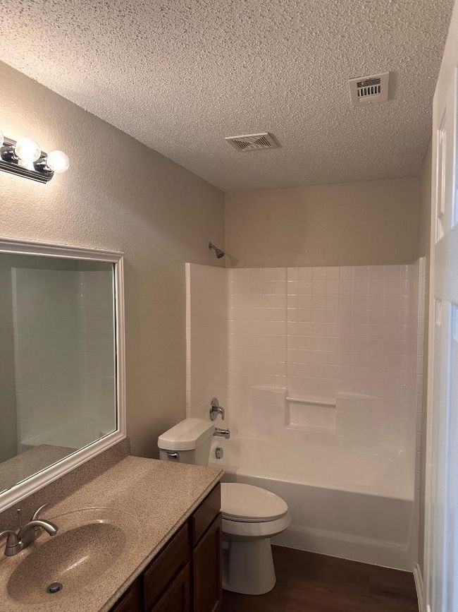 Full bathroom featuring vanity, wood finished floors, toilet, a textured ceiling, and bathtub / shower combination | Image 14