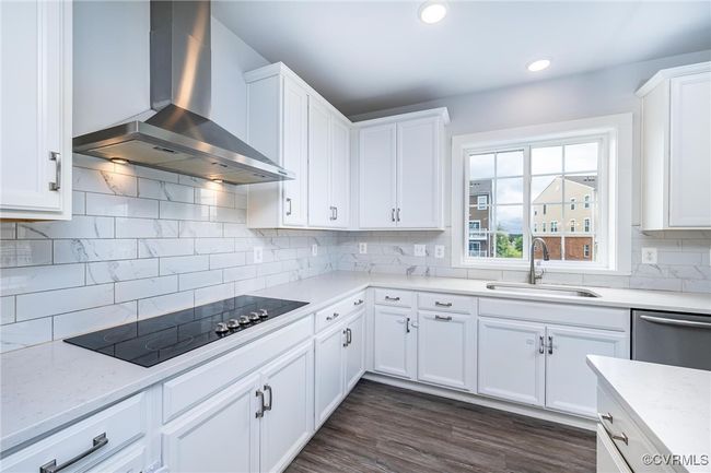 Kitchen featuring wall chimney range hood, black electric stovetop, dishwasher, white cabinetry, and recessed lighting | Image 10