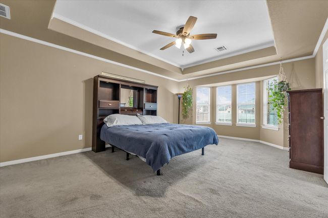 Carpeted bedroom with a tray ceiling, ornamental molding, baseboards, and a ceiling fan | Image 21
