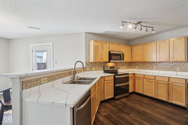 kitchen with stainless steel appliances, a peninsula, a sink, dark wood-type flooring, and a textured ceiling | Image 25