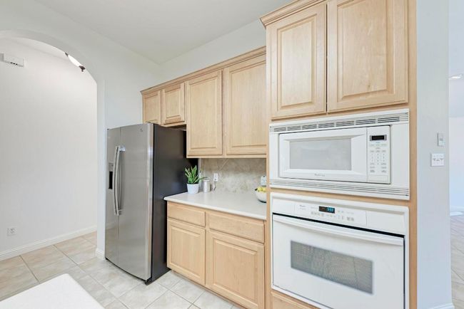 Kitchen featuring tasteful backsplash, arched walkways, light brown cabinets, and white appliances | Image 21