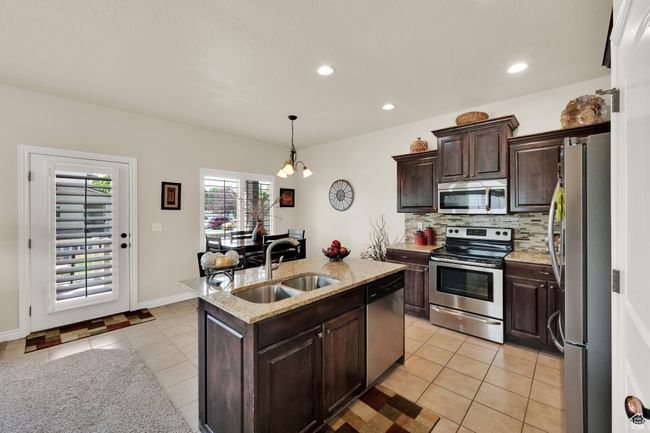 Kitchen with appliances with stainless steel finishes, light tile patterned floors, backsplash, an island with sink, and dark brown cabinetry | Image 8