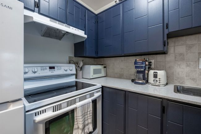 Kitchen featuring freestanding refrigerator, electric stove, under cabinet range hood, white microwave, and blue cabinets | Image 14