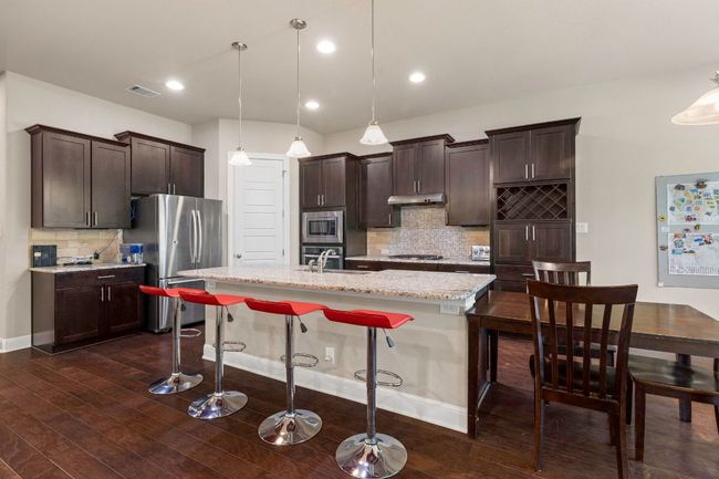 Kitchen featuring stainless steel appliances, decorative backsplash, dark wood finished floors, an island with sink, and recessed lighting | Image 11
