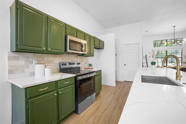 Kitchen featuring appliances with stainless steel finishes, light wood-type flooring, backsplash, green cabinets, and a chandelier | Image 11