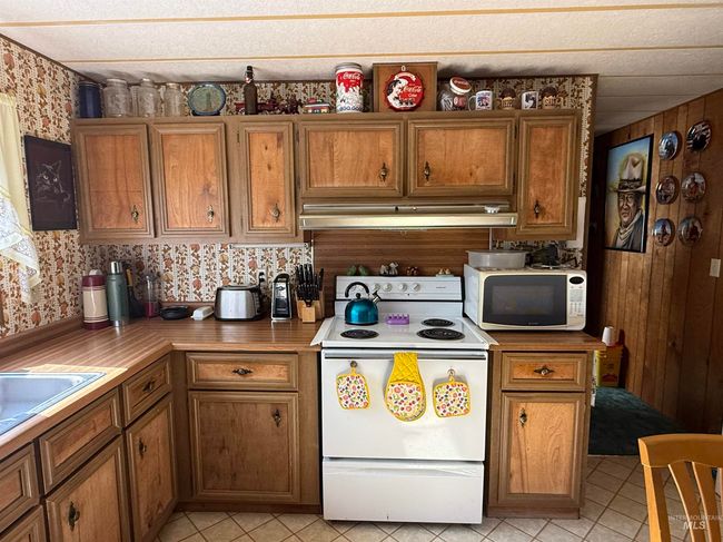 Kitchen featuring white appliances, under cabinet range hood, brown cabinetry, light tile patterned floors, and wallpapered walls | Image 10
