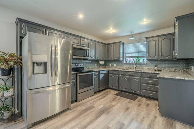Kitchen featuring stainless steel appliances, gray cabinets, decorative backsplash, and light wood-style flooring | Image 8