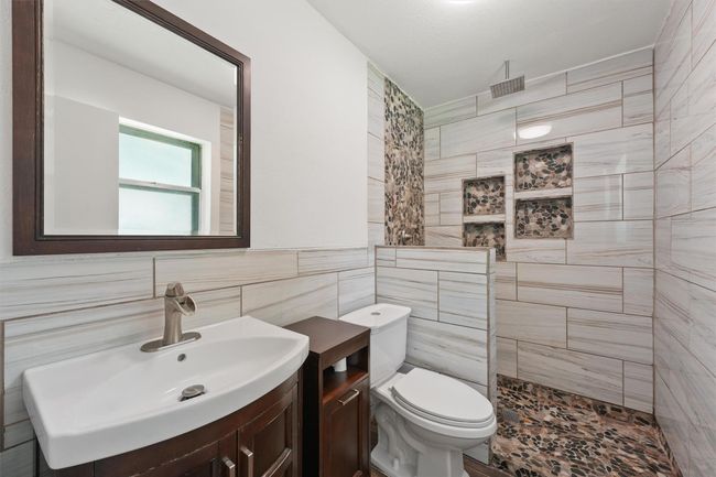 Modern bathroom featuring a sleek sink with a dark wood vanity, large mirror, and a walk-in shower with stylish pebble tile accents. | Image 20