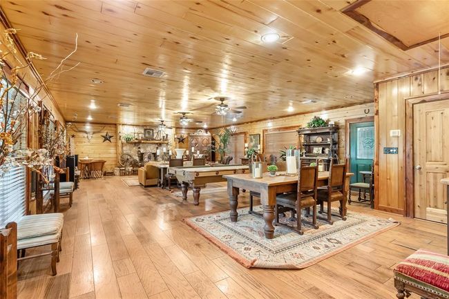 This inviting room features a rustic, wood-paneled interior with ample natural light. It includes a cozy fireplace, a pool table, and a dining area, creating a warm and versatile space for relaxation and entertainment. | Image 34