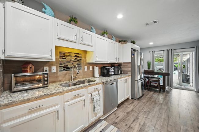 Kitchen featuring appliances with stainless steel finishes, white cabinetry, light stone counters, light wood-style flooring, and recessed lighting | Image 15