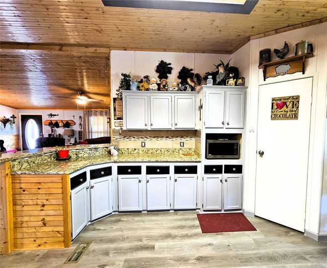 Kitchen with wood ceiling, a peninsula, stainless steel microwave, light wood finished floors, and white cabinets | Image 6