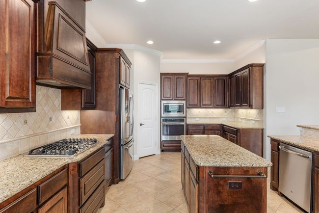 Kitchen featuring crown molding, stainless steel appliances, backsplash, light stone countertops, and a kitchen island | Image 22