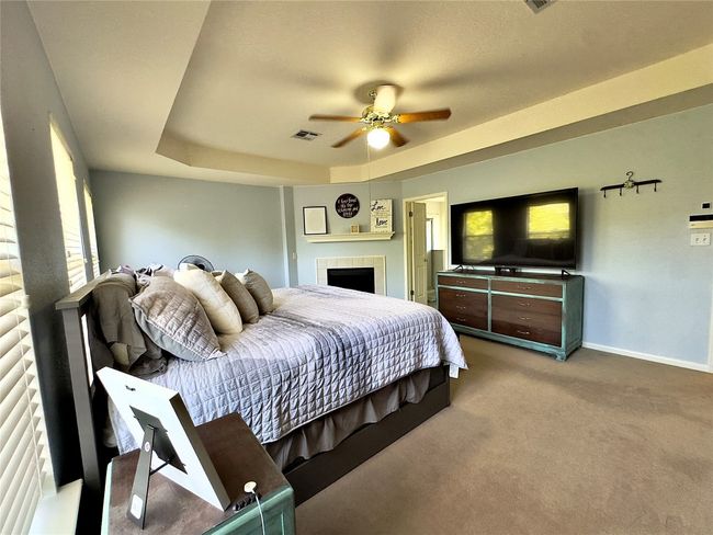 Carpeted bedroom with a tiled fireplace, baseboards, a tray ceiling, and a ceiling fan | Image 31