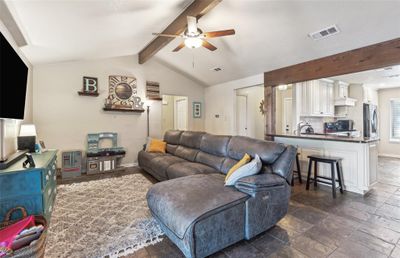 Living room with dark tile patterned flooring, ceiling fan, and vaulted ceiling with beams | Image 1