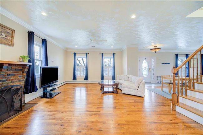 Living area with crown molding, stairway, a brick fireplace, and light wood finished floors | Image 9