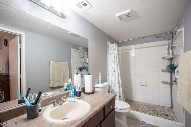 Bathroom with visible vents, a textured ceiling, a tile shower, and toilet | Image 23