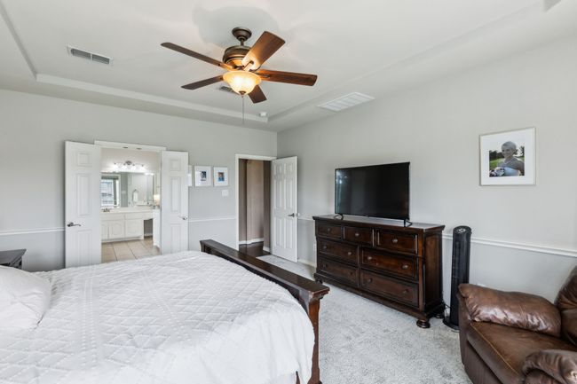 Primary bedroom on first floor with a tray ceiling, new carpet, ceiling fan, and ensuite bath with walk in closet | Image 18