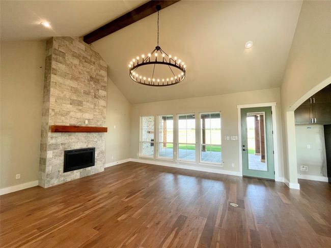 Unfurnished living room with high vaulted ceiling, a chandelier, a stone fireplace, beam ceiling, and dark wood-style flooring | Image 16