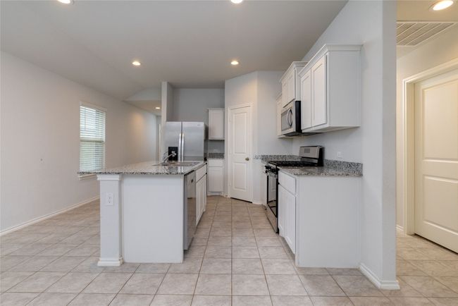 Kitchen with stainless steel appliances, light tile patterned floors, an island with sink, light stone countertops, and recessed lighting | Image 6