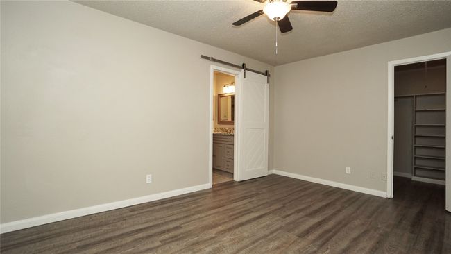 The primary bedroom features a lighted ceiling fan, luxury vinyl plank floors, a walk-in closet, and a barn door entry to the bath | Image 12
