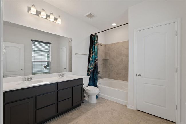Elegant primary bathroom featuring a double vanity, sleek fixtures, and a spacious bathtub with a modern tile surround. | Image 14