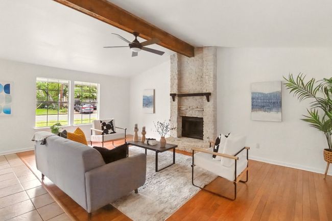 Open-concept living area with vaulted ceilings, a striking wooden beam, and a floor-to-ceiling stone fireplace. Refinished hardwood floors round out the living room space. | Image 5