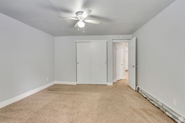 Unfurnished bedroom with light colored carpet, baseboard heating, a closet, baseboards, and a ceiling fan | Image 9