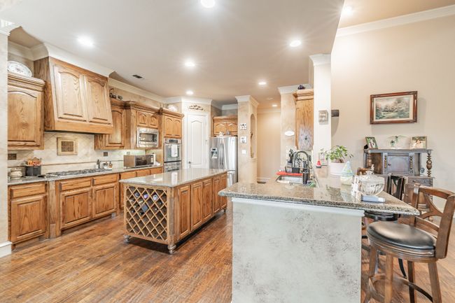 Kitchen featuring appliances with stainless steel finishes, a peninsula, a breakfast bar, backsplash, and dark wood finished floors | Image 19