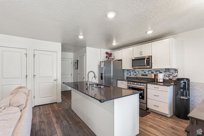 Kitchen featuring stainless steel appliances, dark countertops, dark wood-style flooring, a sink, and a textured ceiling | Image 10