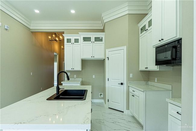 Kitchen with light stone counters, marble finish floor, white cabinets, a sink, and black microwave | Image 9