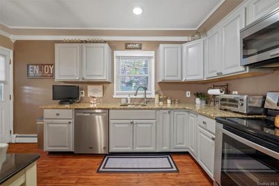 Kitchen featuring white cabinets, a baseboard heating unit, appliances with stainless steel finishes, light hardwood / wood-style flooring, and sink | Image 1