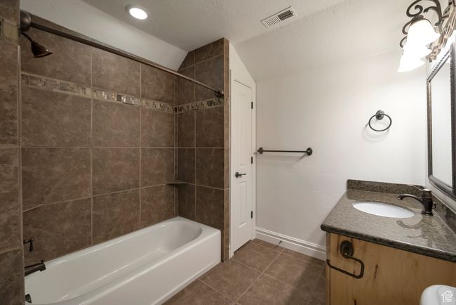 Full bathroom featuring visible vents, vaulted ceiling, shower / washtub combination, vanity, and tile patterned flooring | Image 26