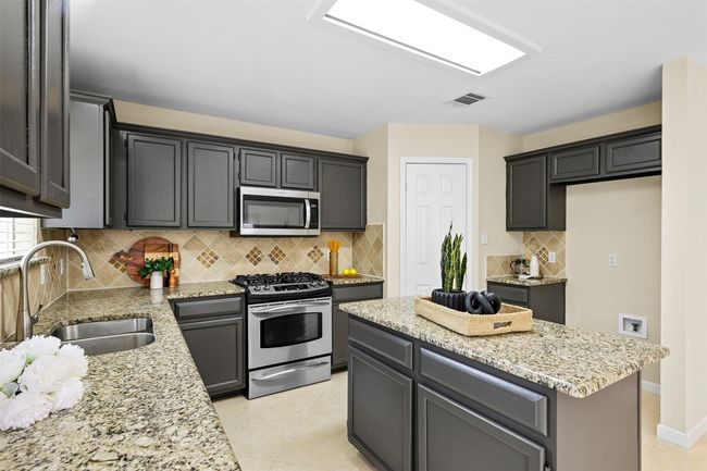 Kitchen with appliances with stainless steel finishes, light stone countertops, a kitchen island, decorative backsplash, and light tile patterned floors | Image 17