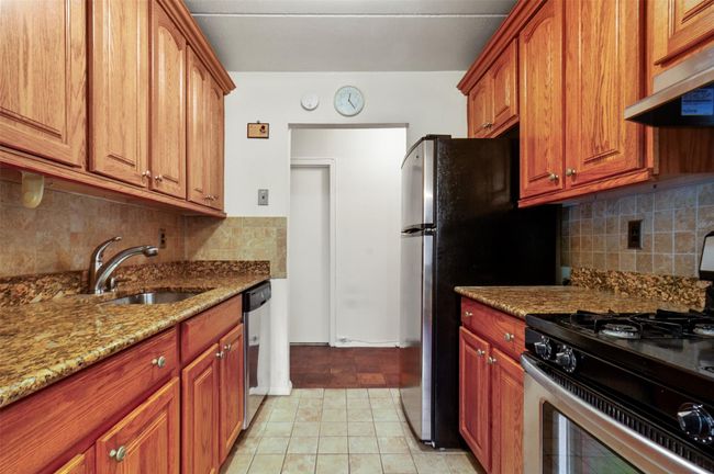 Kitchen featuring gas stove, under cabinet range hood, dishwasher, light stone countertops, and backsplash | Image 15