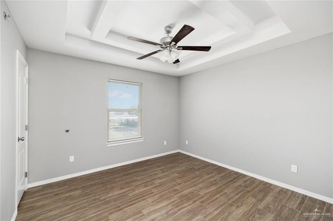 Empty room featuring a raised ceiling, wood finished floors, and a ceiling fan | Image 7