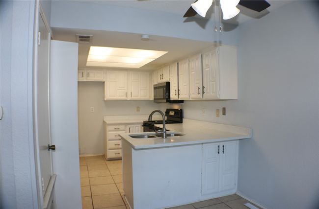 Kitchen with stainless steel microwave, a peninsula, light tile patterned flooring, black range with gas stovetop, and ceiling fan | Image 14
