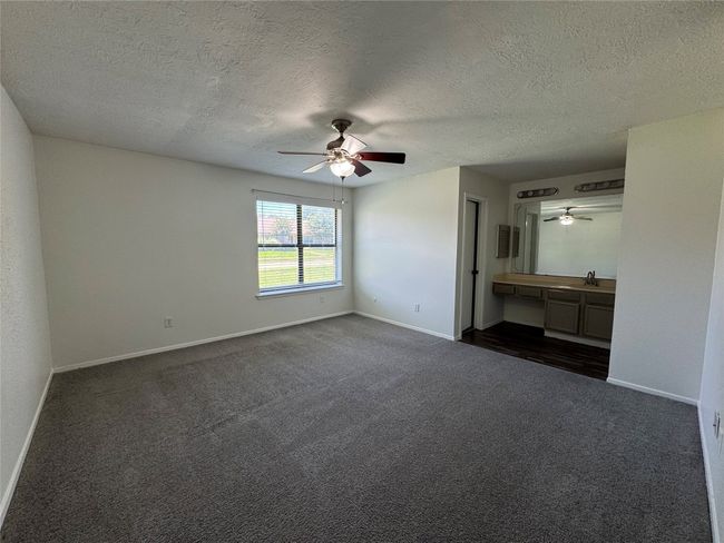 Unfurnished bedroom with dark colored carpet, a textured ceiling, baseboards, a sink, and a ceiling fan | Image 13