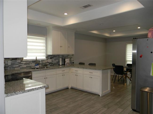 A bright and cozy home office space or breakfast area with three large windows providing natural light. The room has light gray walls and wood-look tile flooring, creating a modern and welcoming atmosphere. | Image 7